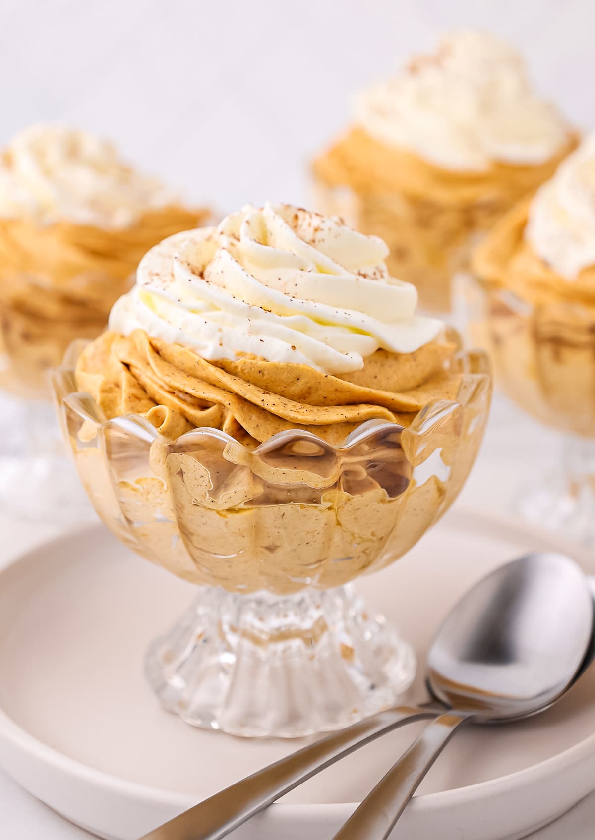 Creamy pumpkin cheesecake mousse topped with cream in a glass dessert bowl with spoons on the side.