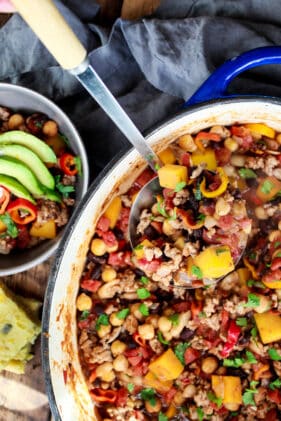 Asian-inspired pork chili in a large pot with a smaller bowl of chili behind topped with fresh guacamole slices.