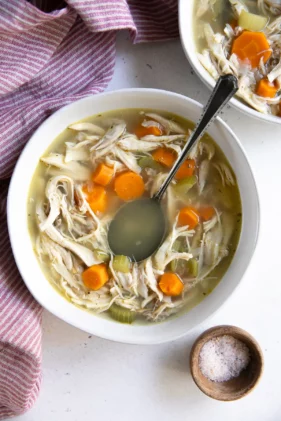 Classic chicken soup in a white bowl with a spoon inserted and a checkered napkin on the side