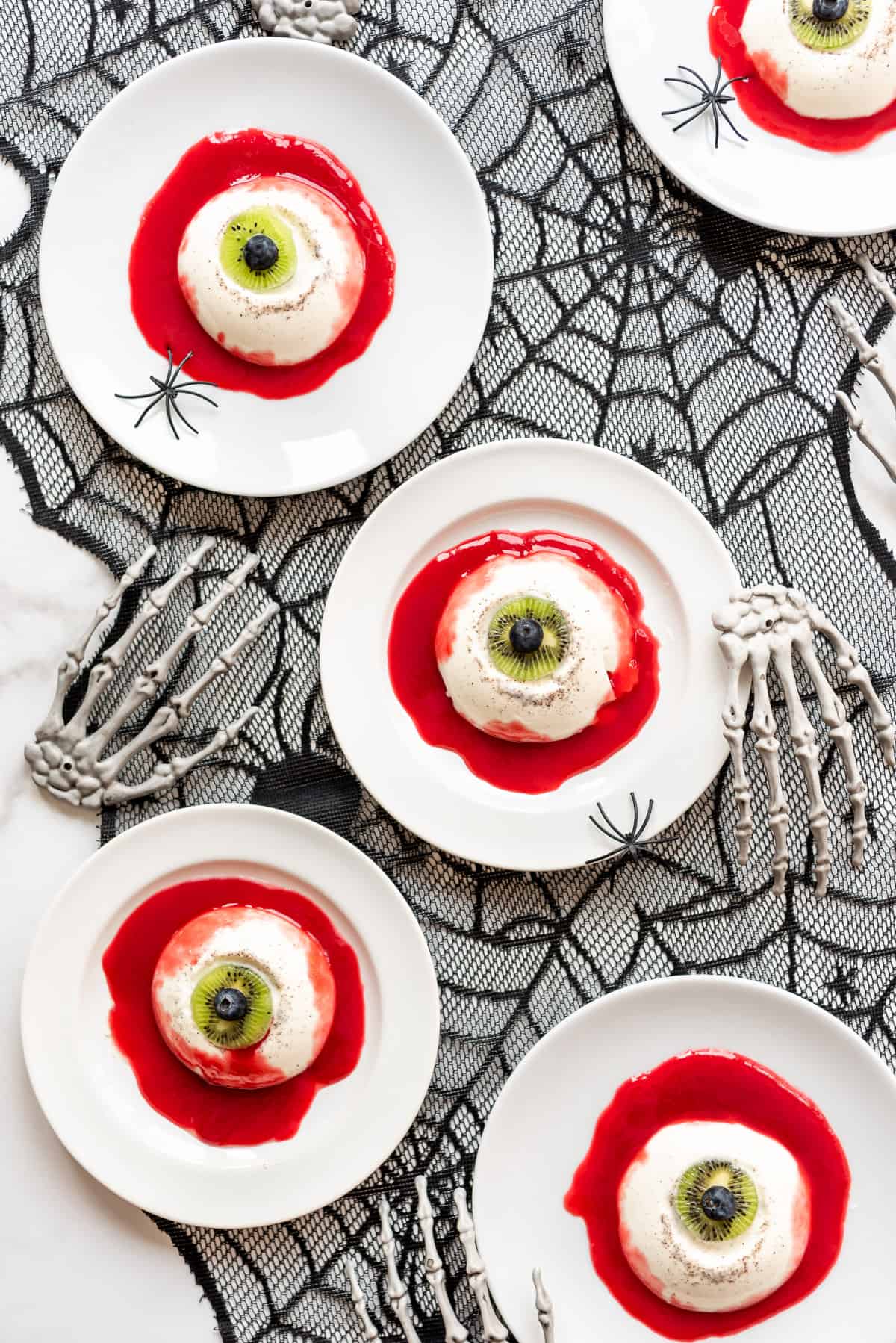 creepy Halloween panna cotta eyeballs made with jello and lychee eyeballs on white plates on top of a spider web place mat