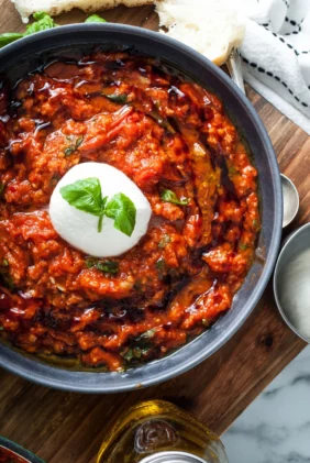 A gray bowl of vibrant and chunky Italian tomato and bread soup topped with burrata cheese on a wooden board