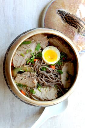 Pork soup with soba noodles in a dark soup bowl topped with a soft boiled egg.