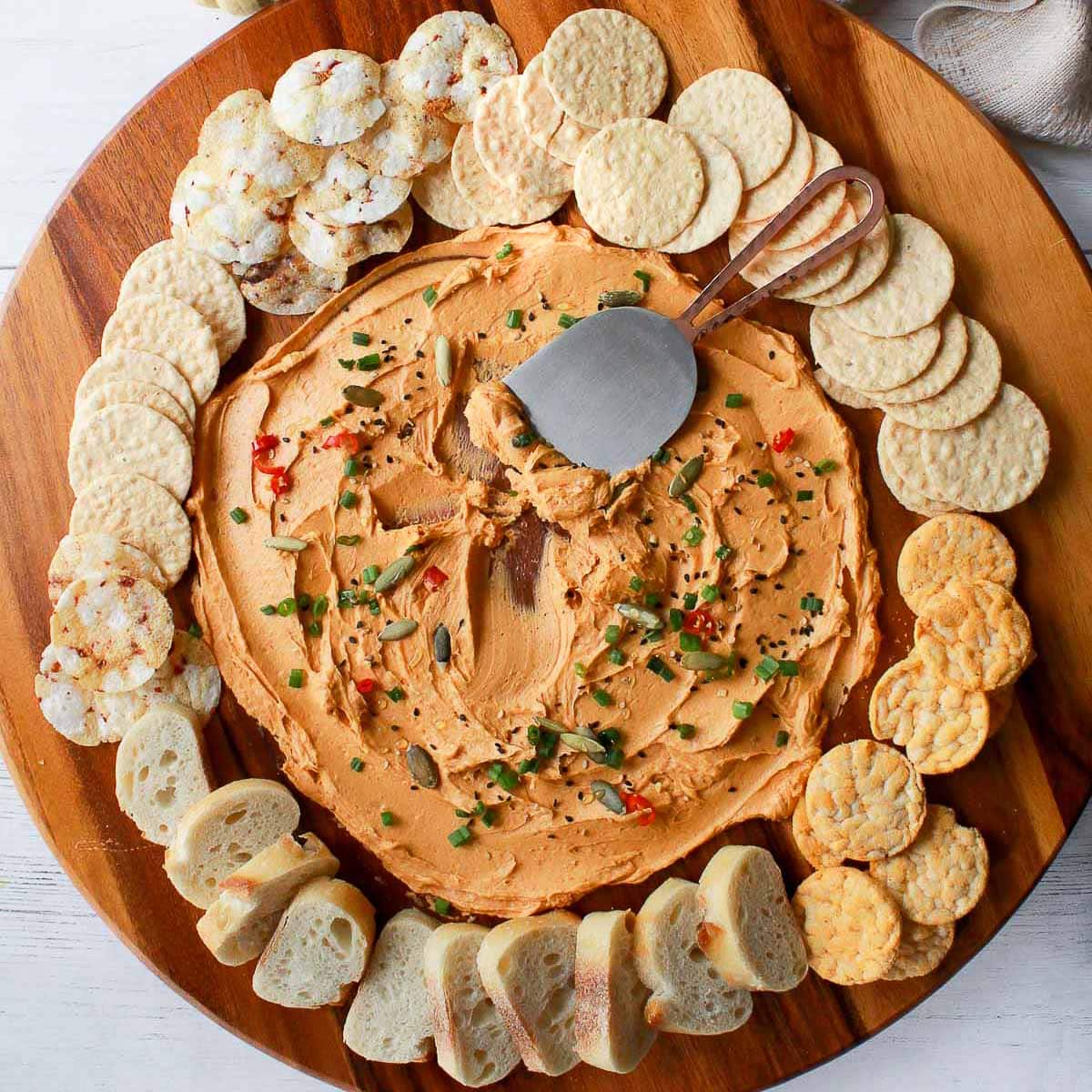 a miso butter board on a round wooden board surrounded by crackers and bread with baby pumpkins and a napkin on the side