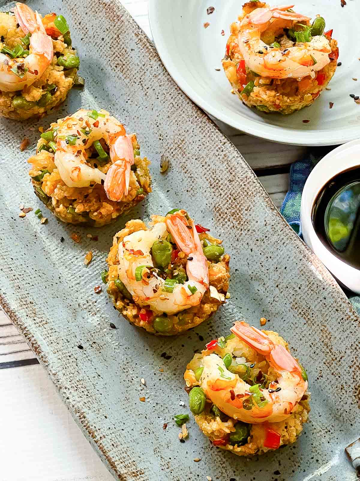 fried rice cups topped with shrimp on a long gray serving plate with soy sauce on the side and a white plate with another fried rice cup