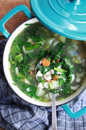 a large blue pot of Thai Clear Soup with a ladle inserted in the pot placed on top of a wooden board