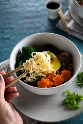 A bowl of turkey meatball ramen noodle soup in a white bowl with a pair of chopsticks lifting up the noodles