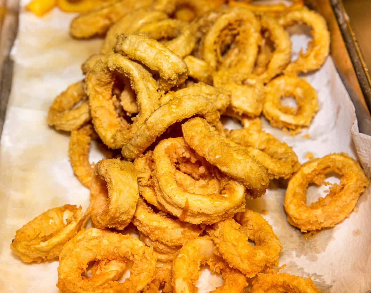 Fried calamari rings draining on a white paper towel on top of a tray.