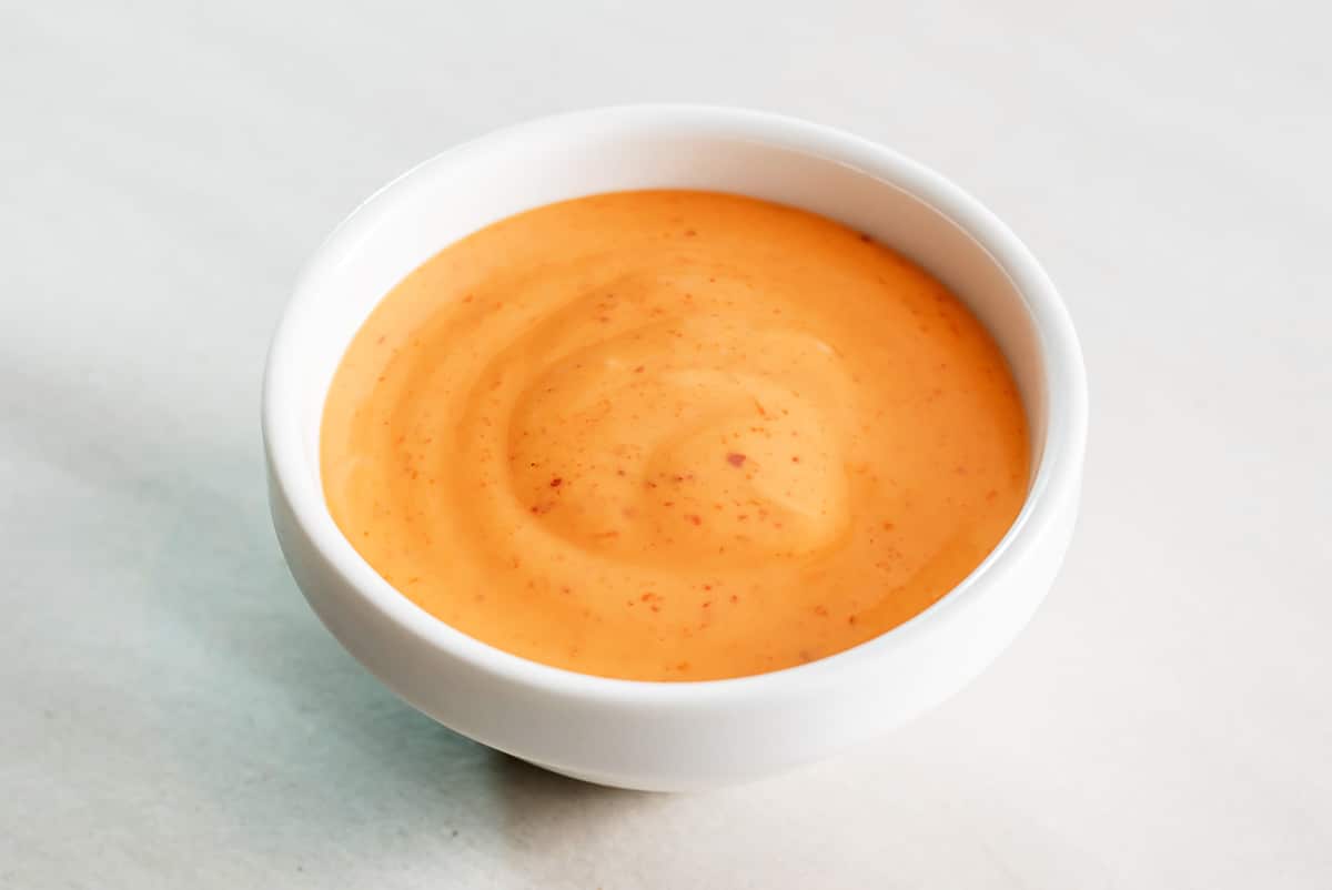 a small white bowl filled with a spicy aioli dipping sauce on a white surface