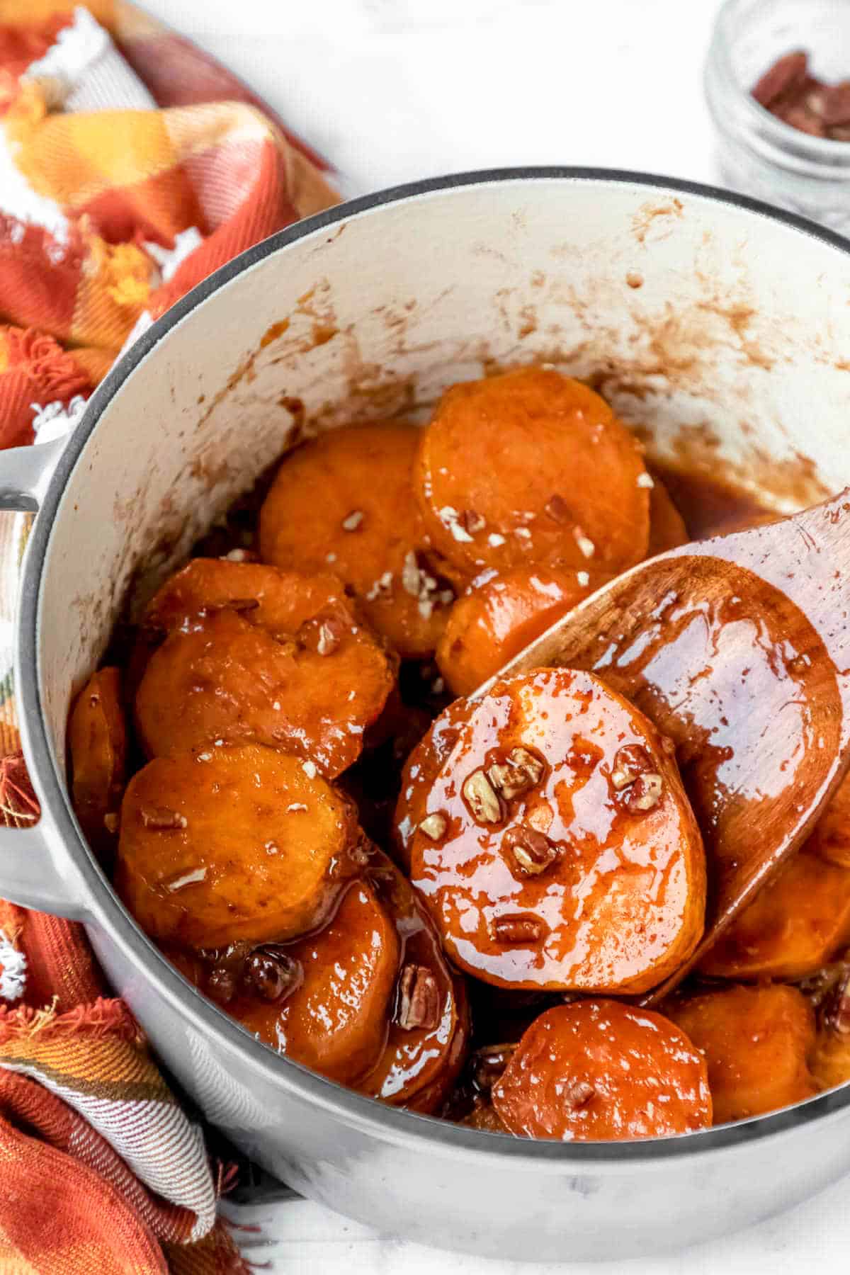 Slices of candied sweet potatoes baked in a white ceramic pot with a wooden spoon.