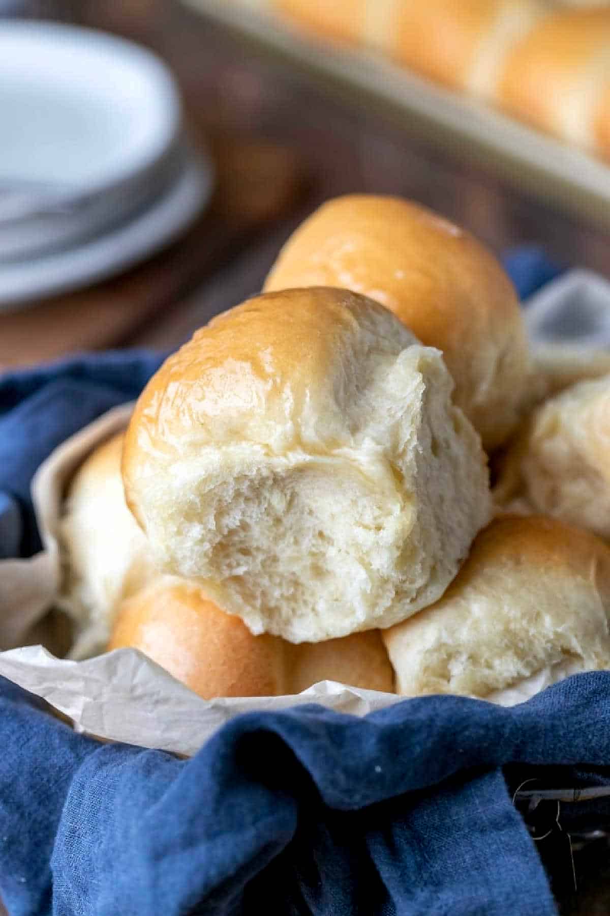 Fluffy homemade dinner rolls stacked in a bread basket lined with a blue linen napkin.