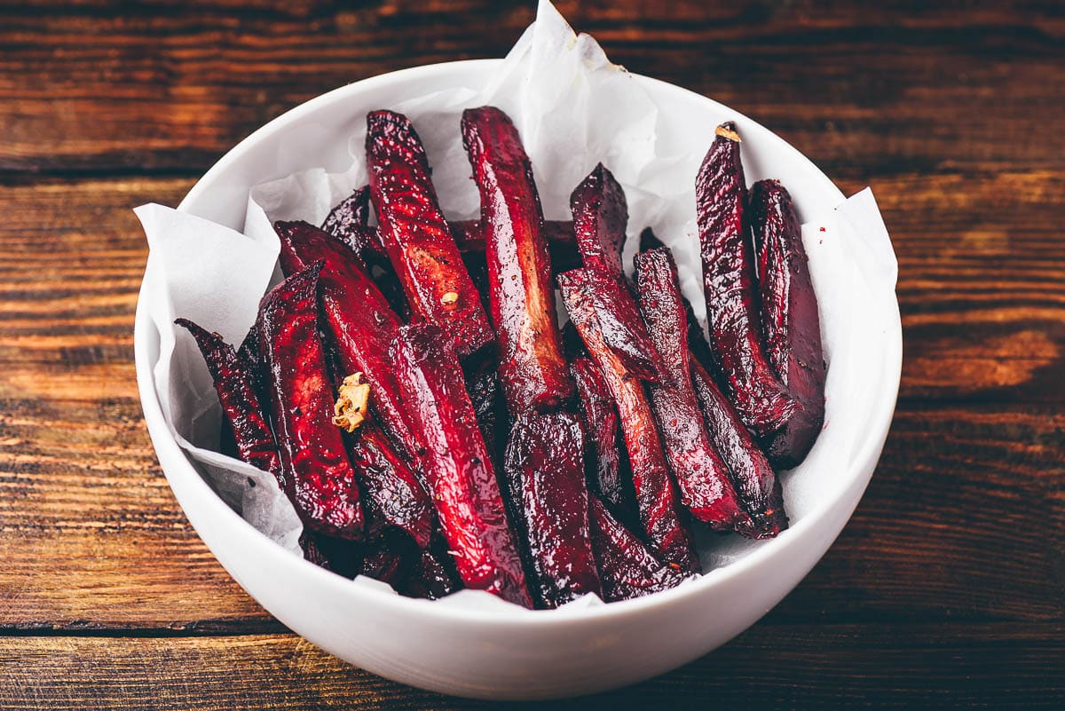 Roasted beet fries holiday side dish in a white bowl lined with parchment paper on top of a wooden board.