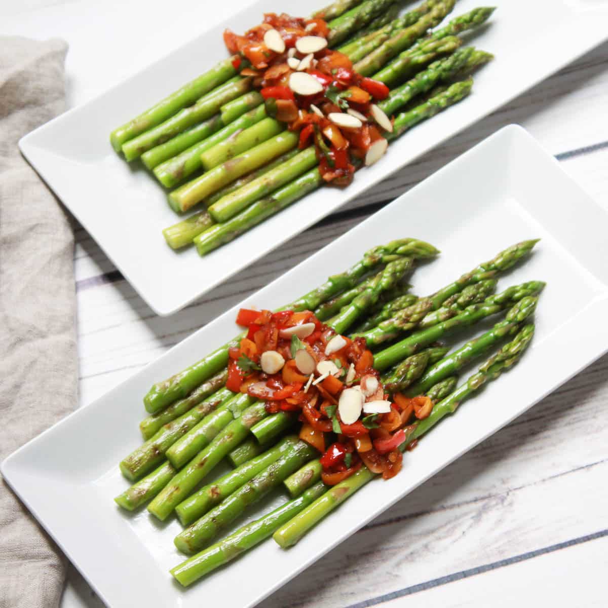 Roasted asparagus spears side dish on a long white plates topped with a sweet and spicy pepper sauce on top of a white wooden board.