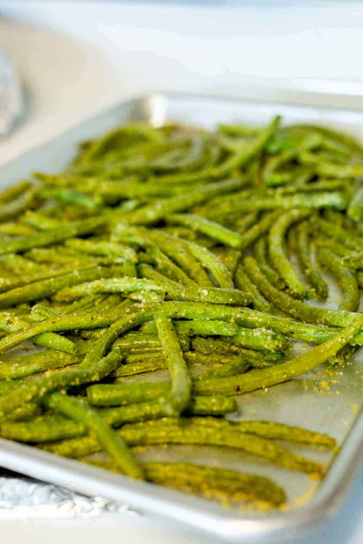 Roasted parmesan green beans right out of the oven on a silver baking sheet.