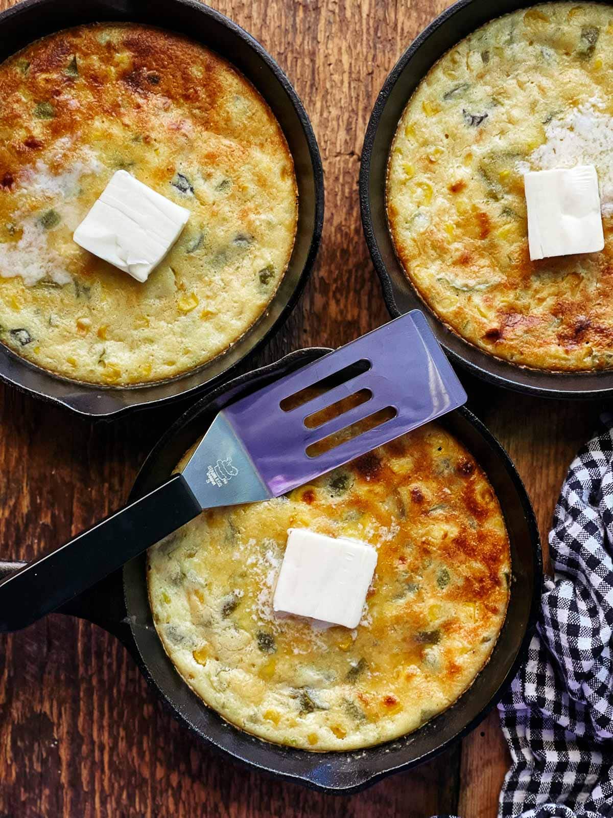 Three small cast iron pans filled with jalapeño cornbread and topped with a pat of melting butter on top of a wooden board.