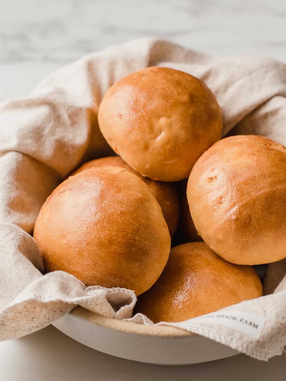 Sourdough sweet potato rolls piled in a bread basket lined with a linen napkin.