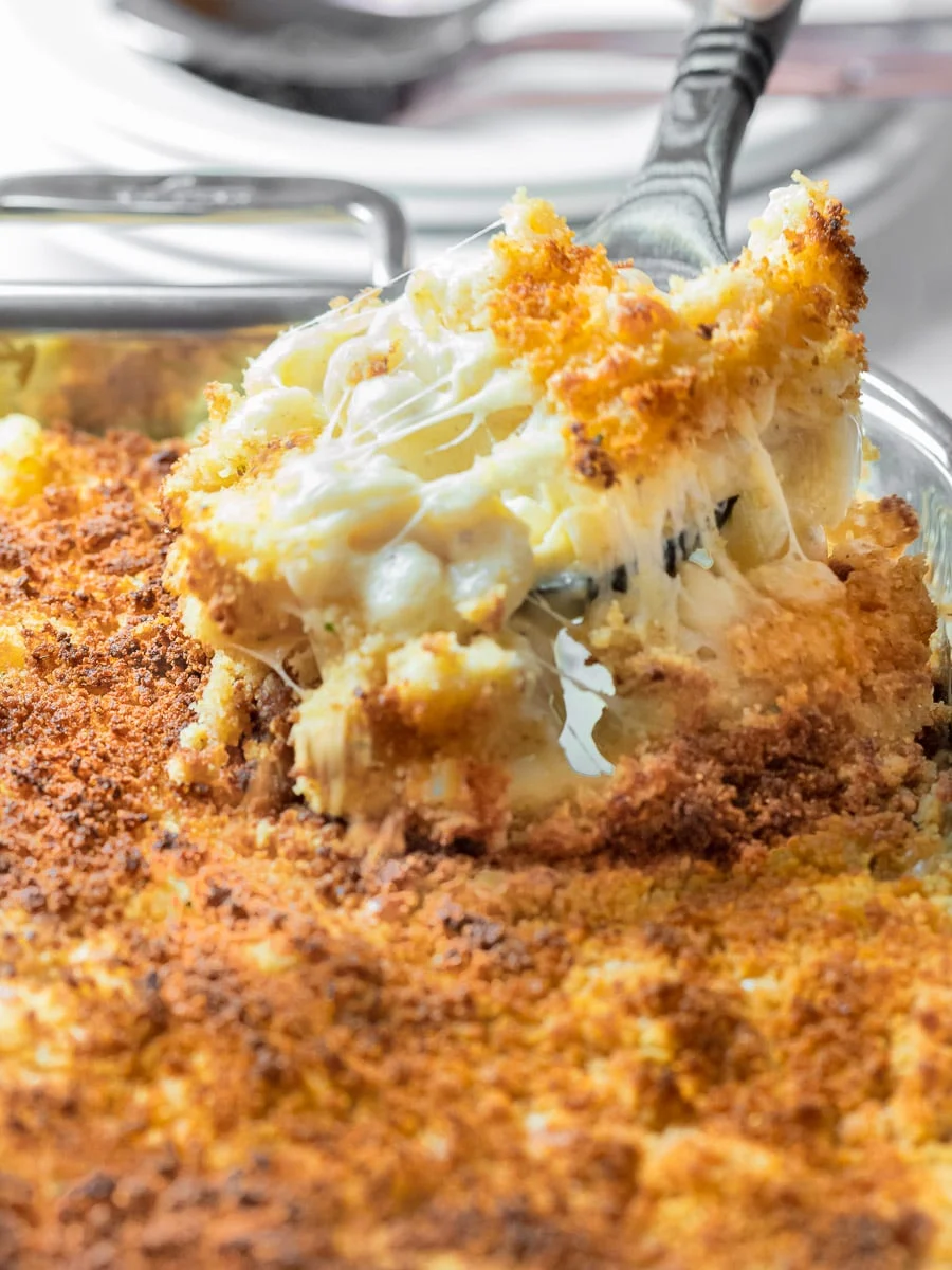 Cheesy southern baked mac and cheese being lifted by a large spoon from a clear pyrex serving pan.