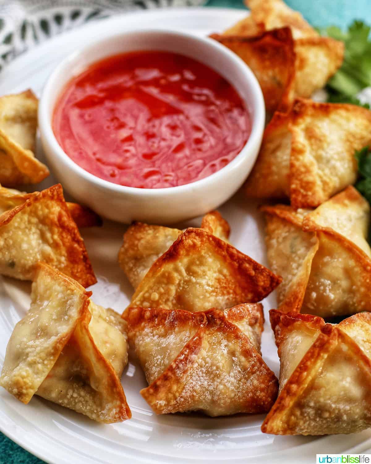 Air fryer crab rangoon lined up on a plate with a small white bowl of sweet chili dipping sauce in the middle of the plate.
