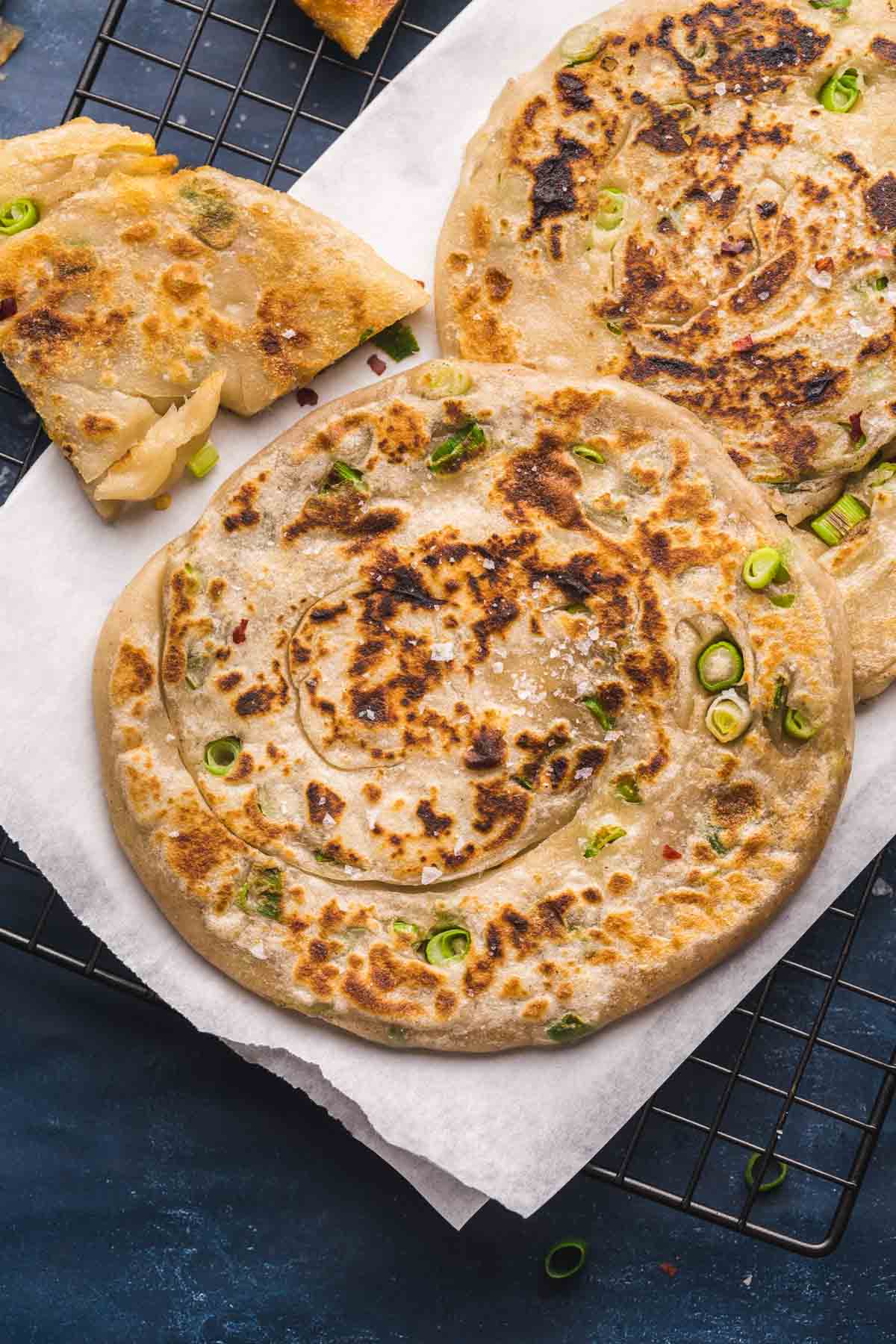 Chinese scallion pancakes on a white plate, on top of a black baking rack.