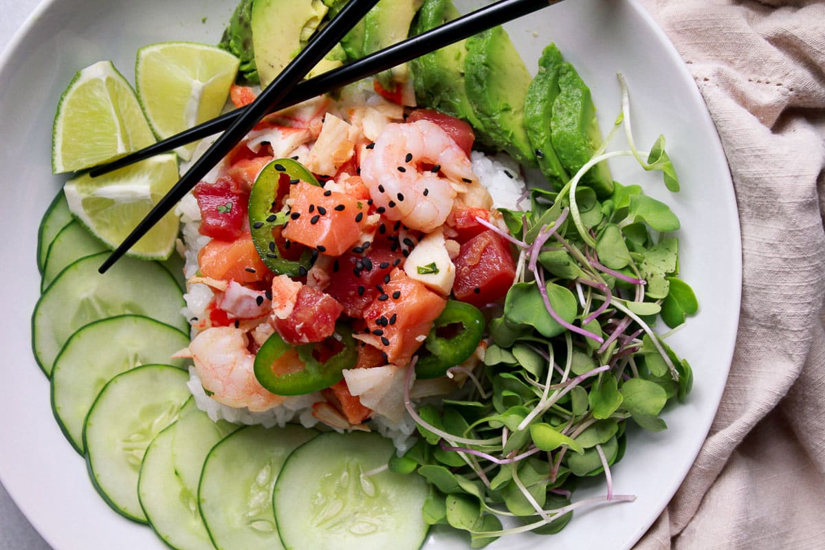 Cubed sushi-grade fish, crab and shrimp in this mixed seafood poke bowl with sliced cucumbers, avocados, and sprouts on the side.