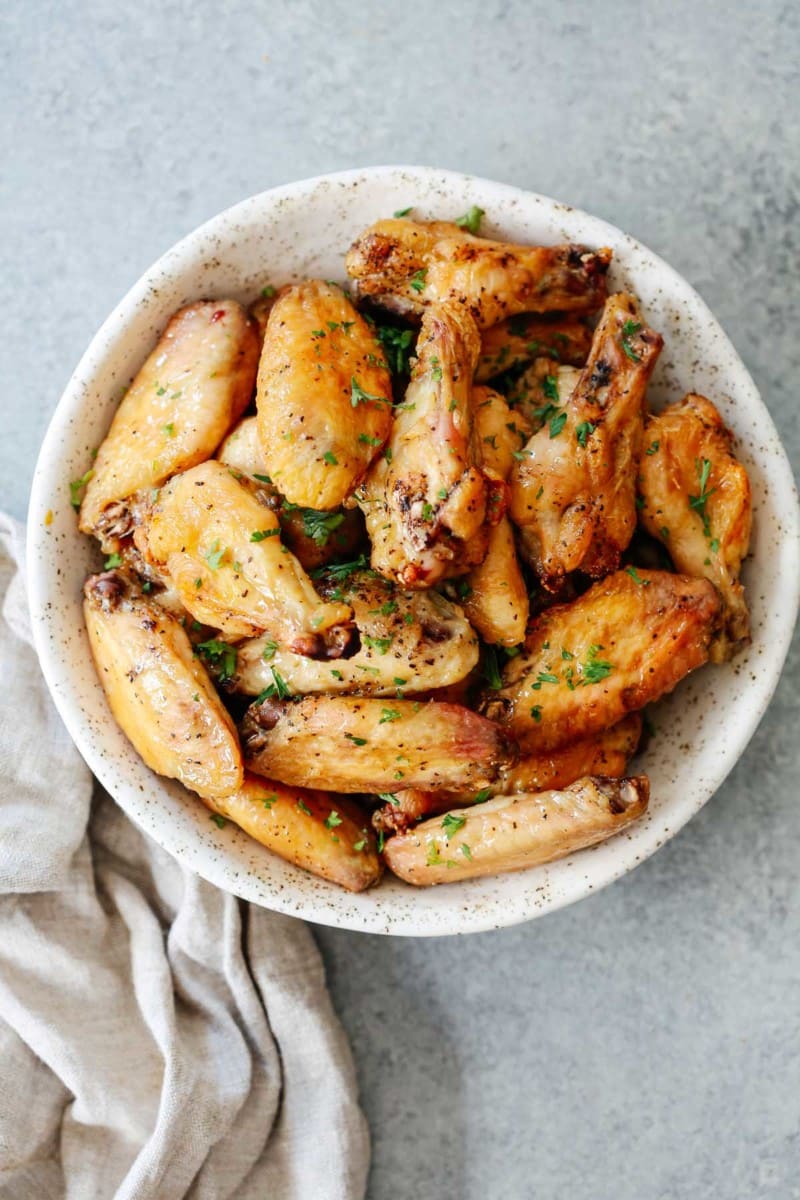 A white bowl filled with Chinese salt and pepper chicken wings on a gray surface with a linen napkin on the side.