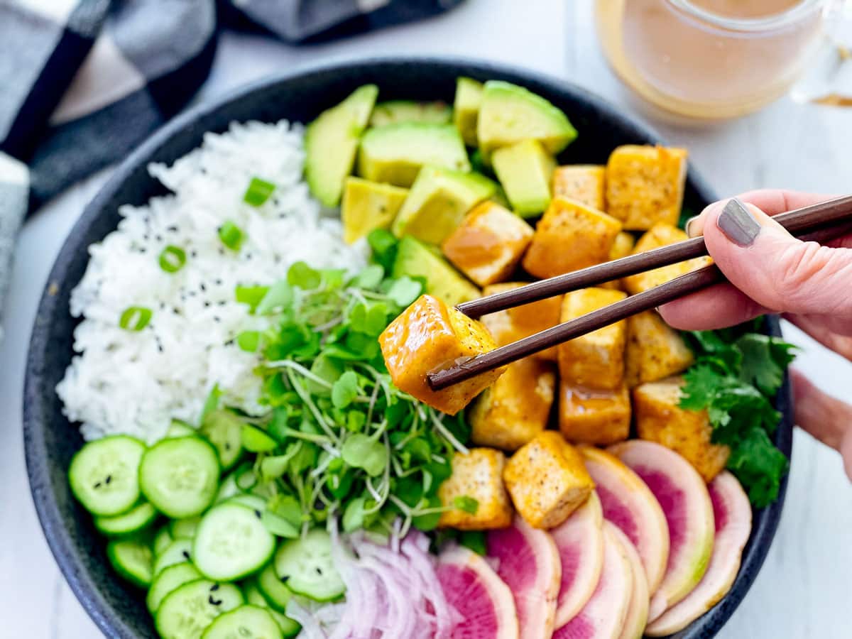 Seared miso tofu in a bowl with white rice, avocado chunks, crispy cucumber slices, vibrant sliced rainbow radishes, and sprouts.