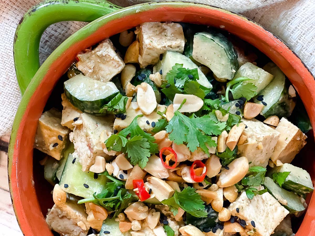 A green bowl filled with a vibrant spicy Asian tofu salad with cucumbers, cilantro and peanuts.