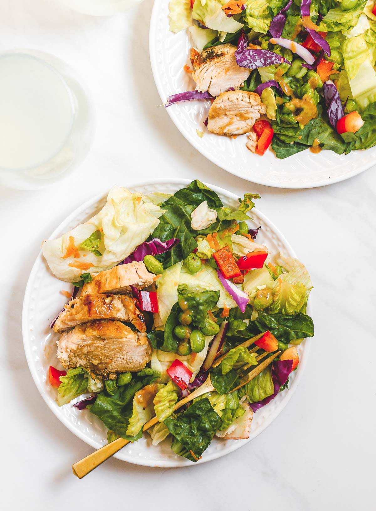 Two white bowls with Spicy Thai Salad with Chicken with a fork on top placed on top of a marble surface.