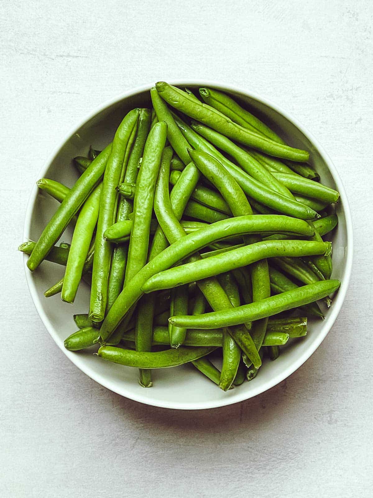 Fresh green beans in a round white bowl.