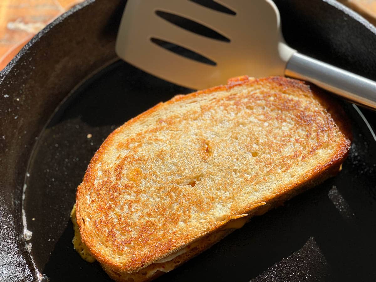 A golden grilled cheese sandwich in a cast iron pan with a spatula on the side