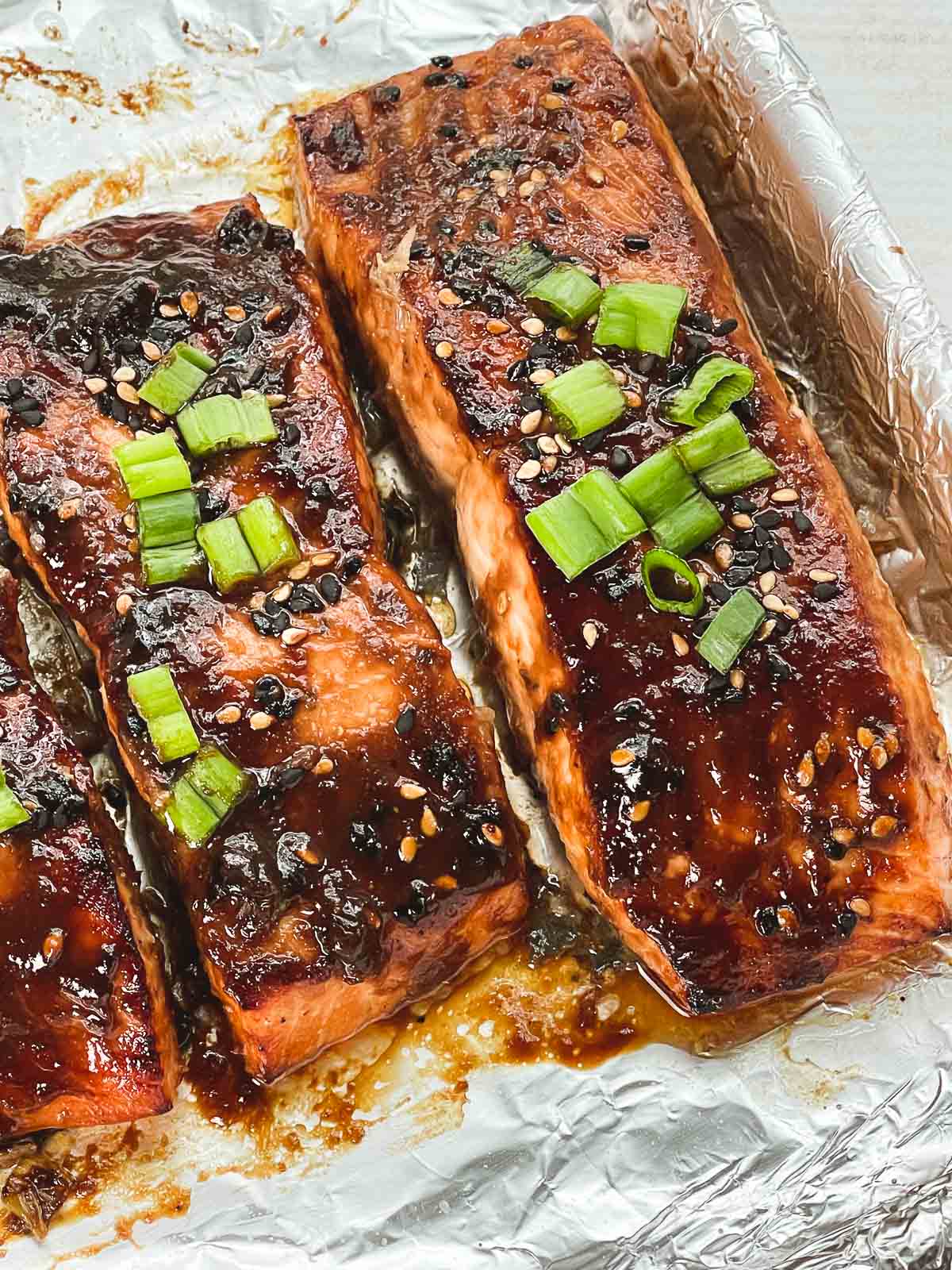 Broiled miso glazed salmon filets topped with chopped green onions on a baking sheet lined with foil.