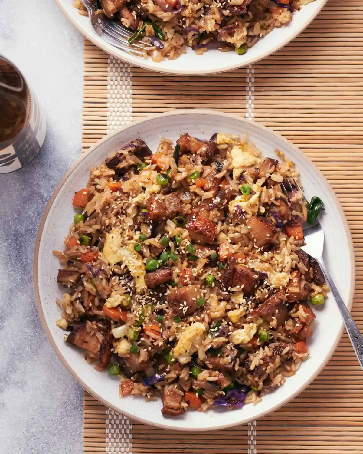 Pork belly fried rice on a two round white plates with forks, on top of a bamboo mat.