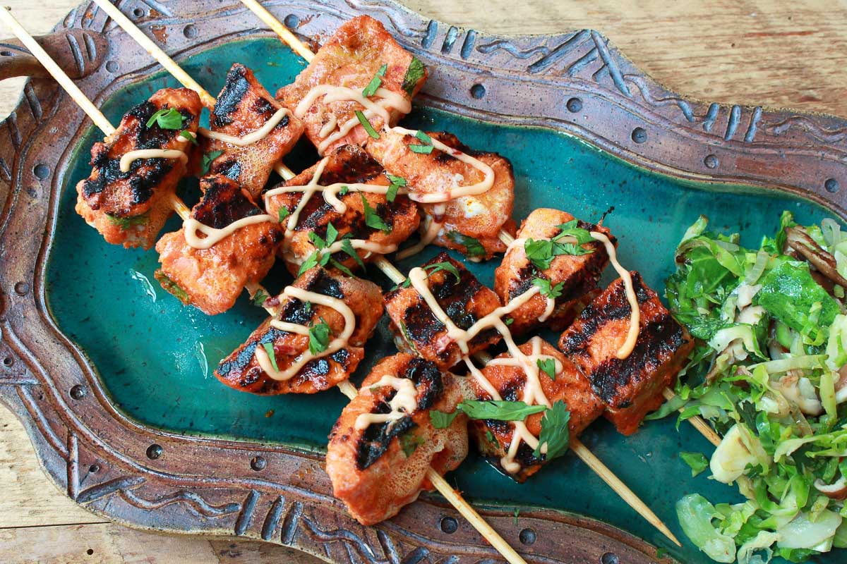 Skewered, grilled red curry salmon kebabs on a green platter with a brussels sprouts salad on the side.