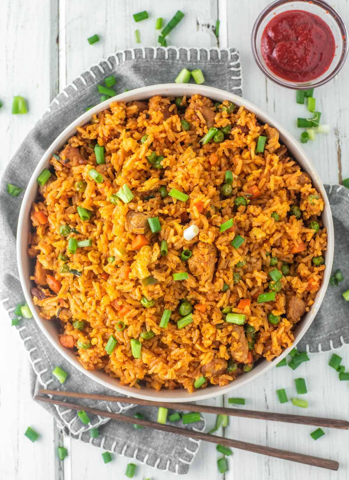 Gochujang Fried Rice in a large white bowl on top of a gray napkin with wooden chopsticks and gochujang sauce on the side.