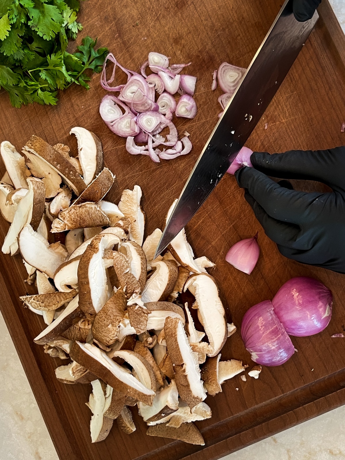 Slicing shallots on a cutting board with sliced shiitake mushrooms, and cilantro on the side.