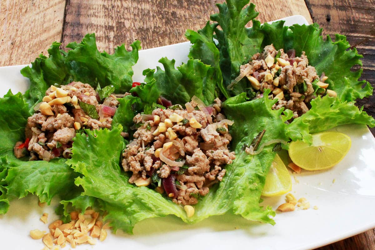 Turkey lettuce wraps, Thai larb, on a long white platter with lime wedges on the side, on top of a wooden board.