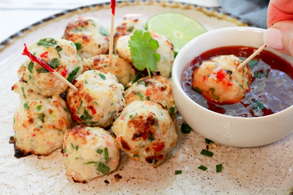 Spicy Baked Shrimp Balls stacked on a round plate with a single meatball being dipped into a bowl of sweet chili sauce.