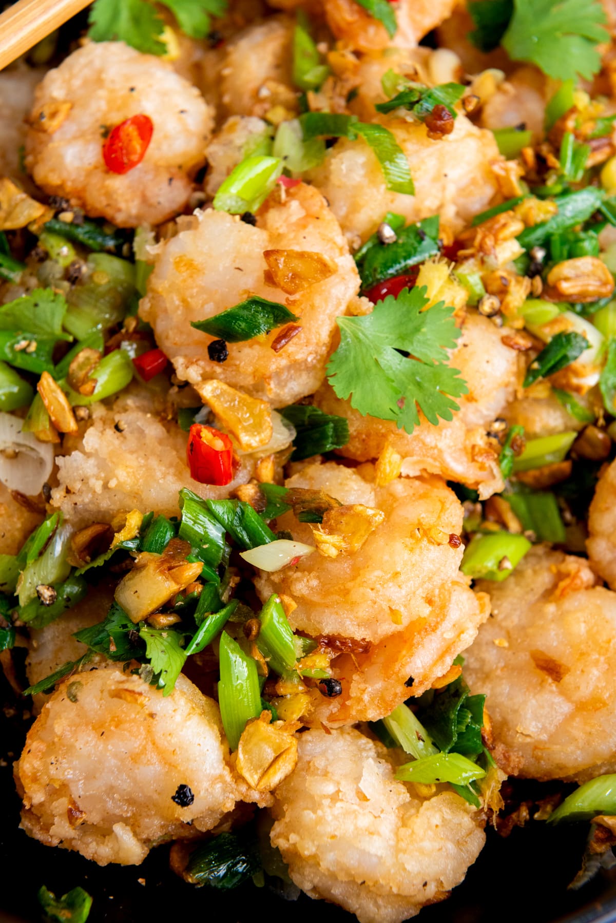 A close-up image of Chinese salt and pepper shrimp with sautéed vegetables and herbs.