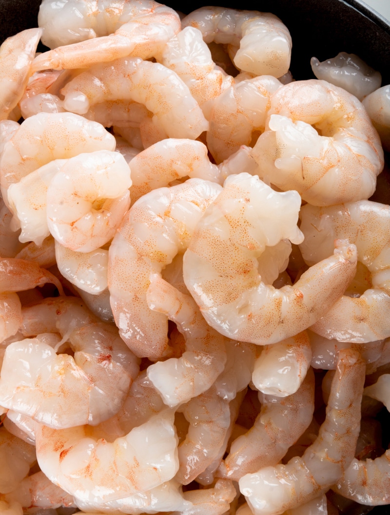A close-up image of raw pink shrimp stacked on top of each other.