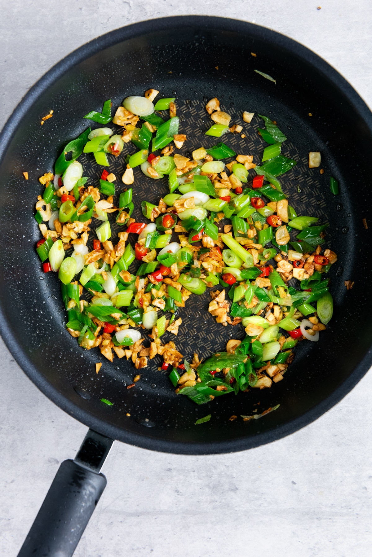 Peppers, scallions, ginger, and garlic being sautéed in a frying pan.