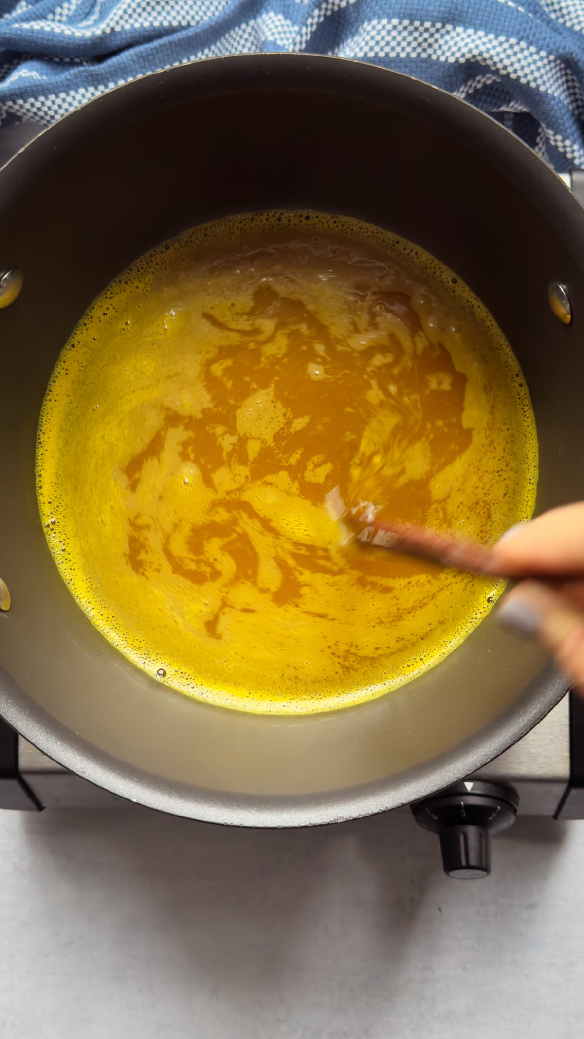 Broth for Chinese egg drop soup being stirred in a pot on top of a gray surface with a blue napkin on the side.