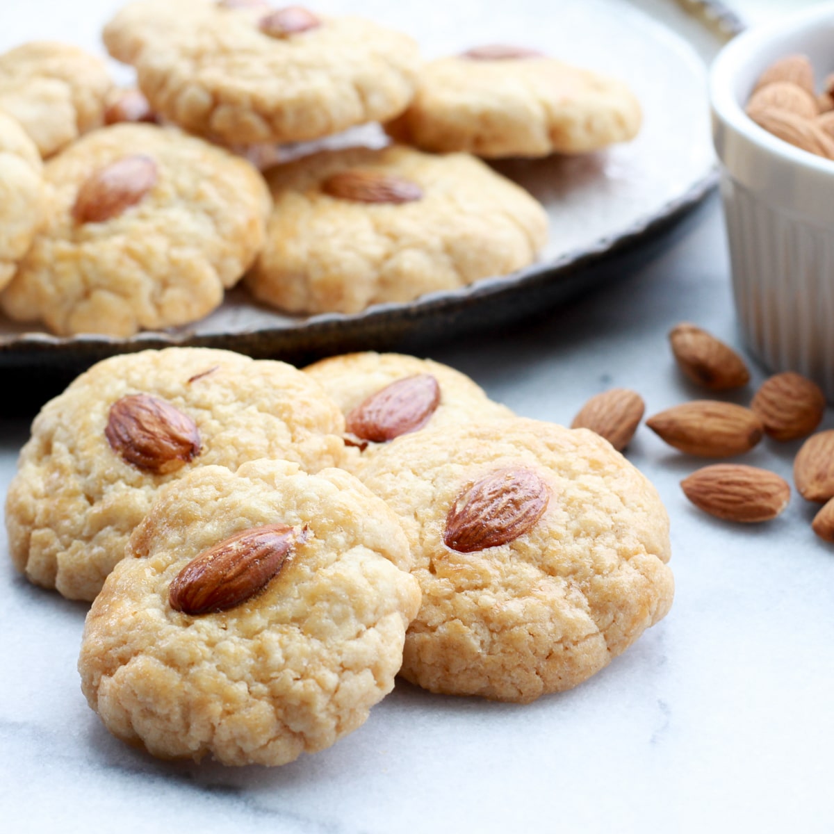 Chinese almond cookies stacked on a round plate, with a small bowl of whole almonds on the side.