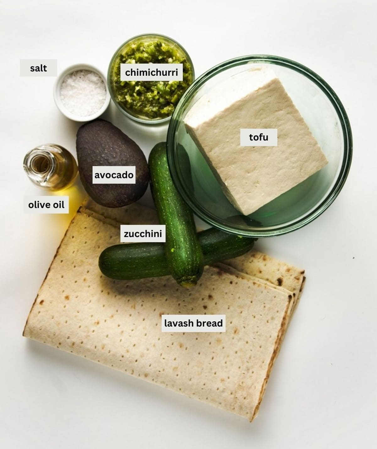 Labeled ingredients for making grilled tofu and zucchini wraps on top of a white surface.