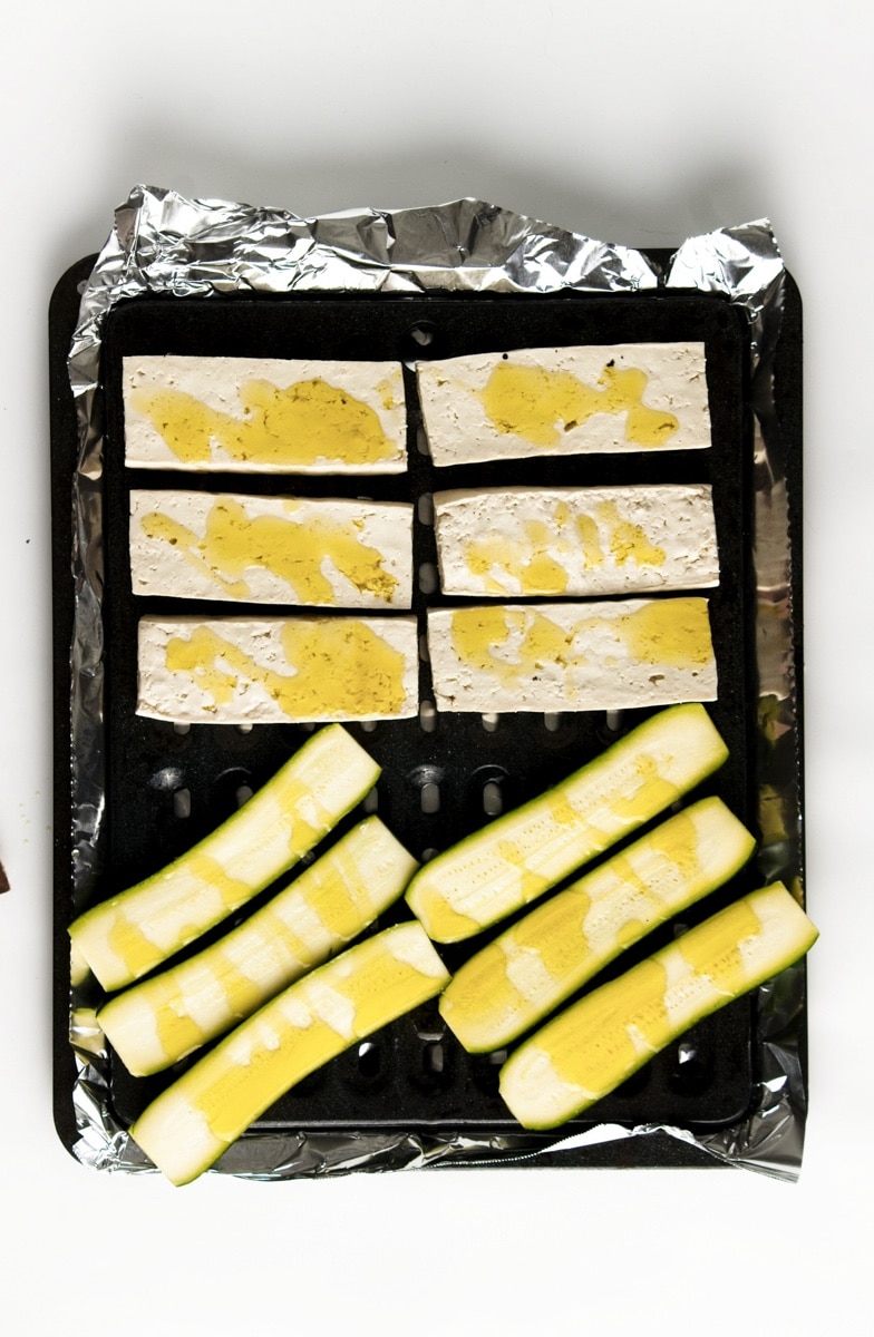 Sliced tofu and zucchini on a grill oven tray ready for the oven.