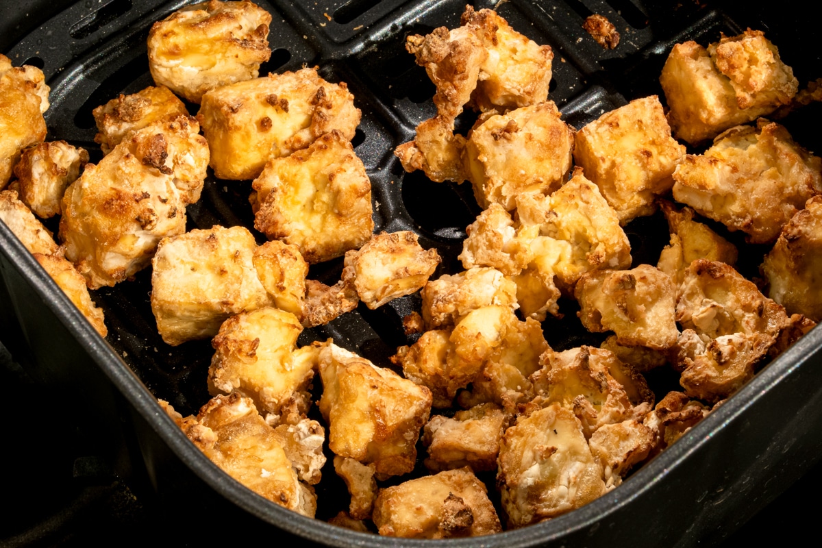 Golden and crispy tofu cubes in an air fryer tray.