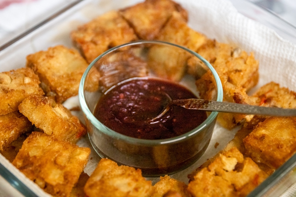Crispy air-fried tofu cubes on a plate with a dipping sauce in the middle.