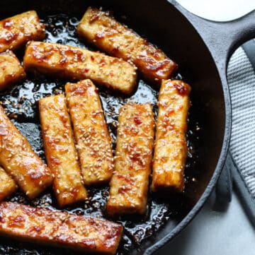 Thick tofu strips cooking in a black cast iron pan.