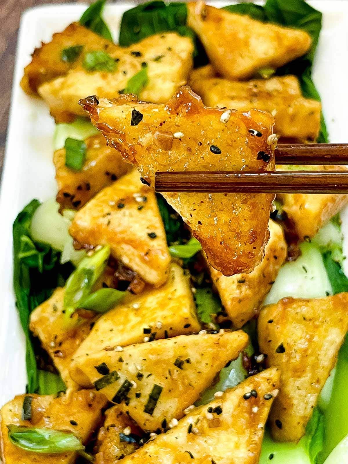 Crispy Tofu Steaks with Bok Choy triangles on a white plate with chopsticks.