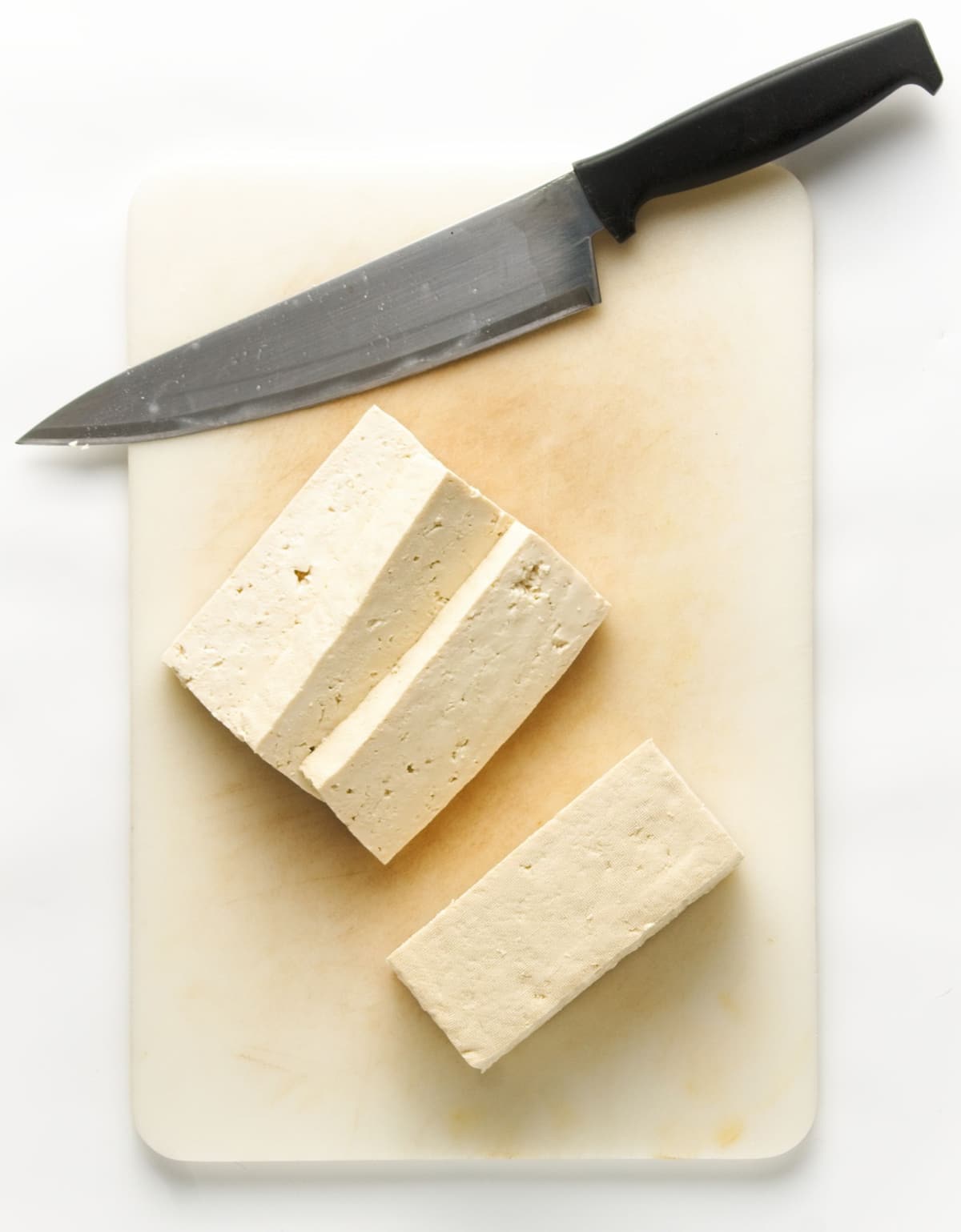 Sliced tofu on a white cutting board with a chefs knife on the side.