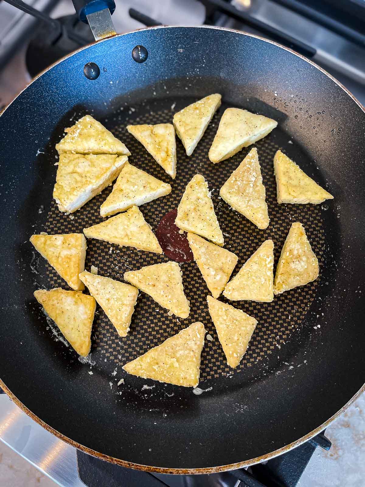Tofu triangles crisping in a frying pan.