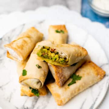 Air Fryer avocado egg rolls stacked on a white plate.